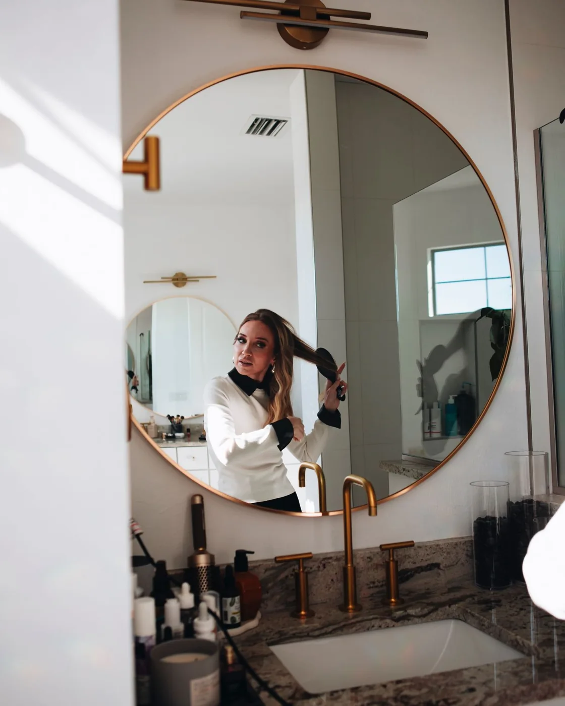 Woman brushing her hair in a bathroom with a round mirror