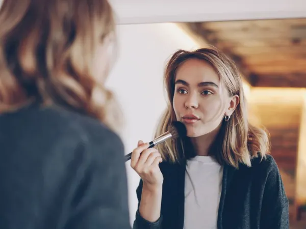 Woman applying makeup in front of a mirror