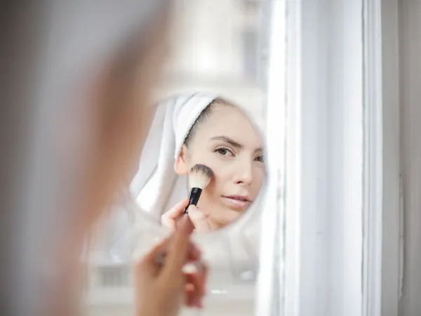 Woman using a makeup brush in a mirror at home