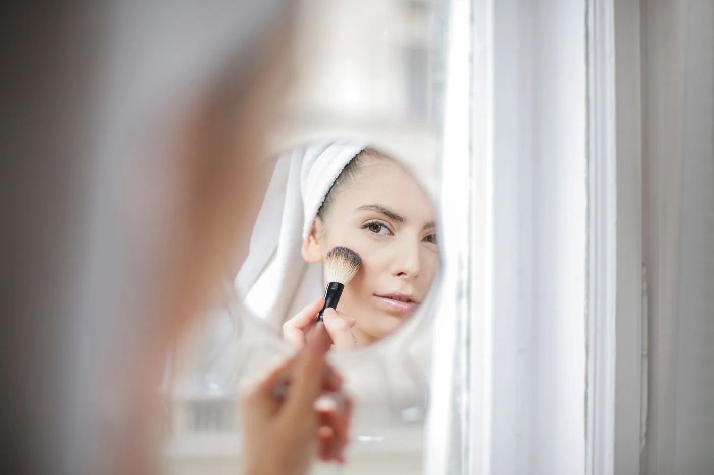Woman using a makeup brush in a mirror at home