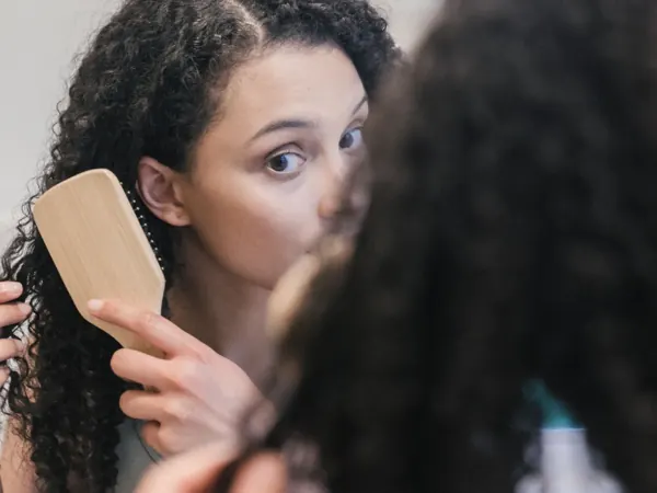 Woman brushing curly hair in front of a mirror