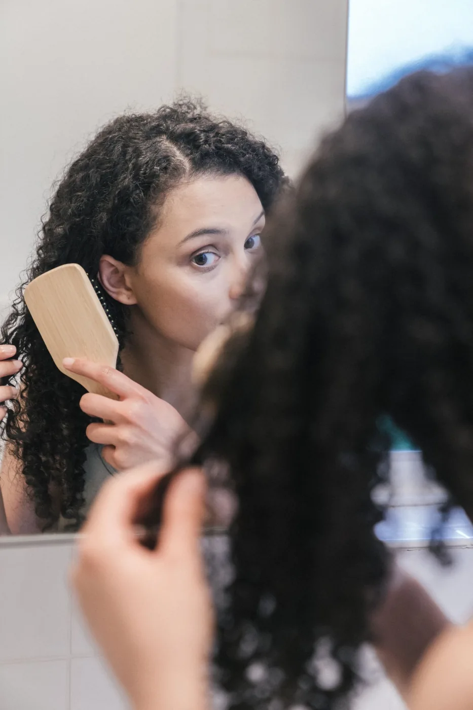 Woman brushing curly hair in front of a mirror