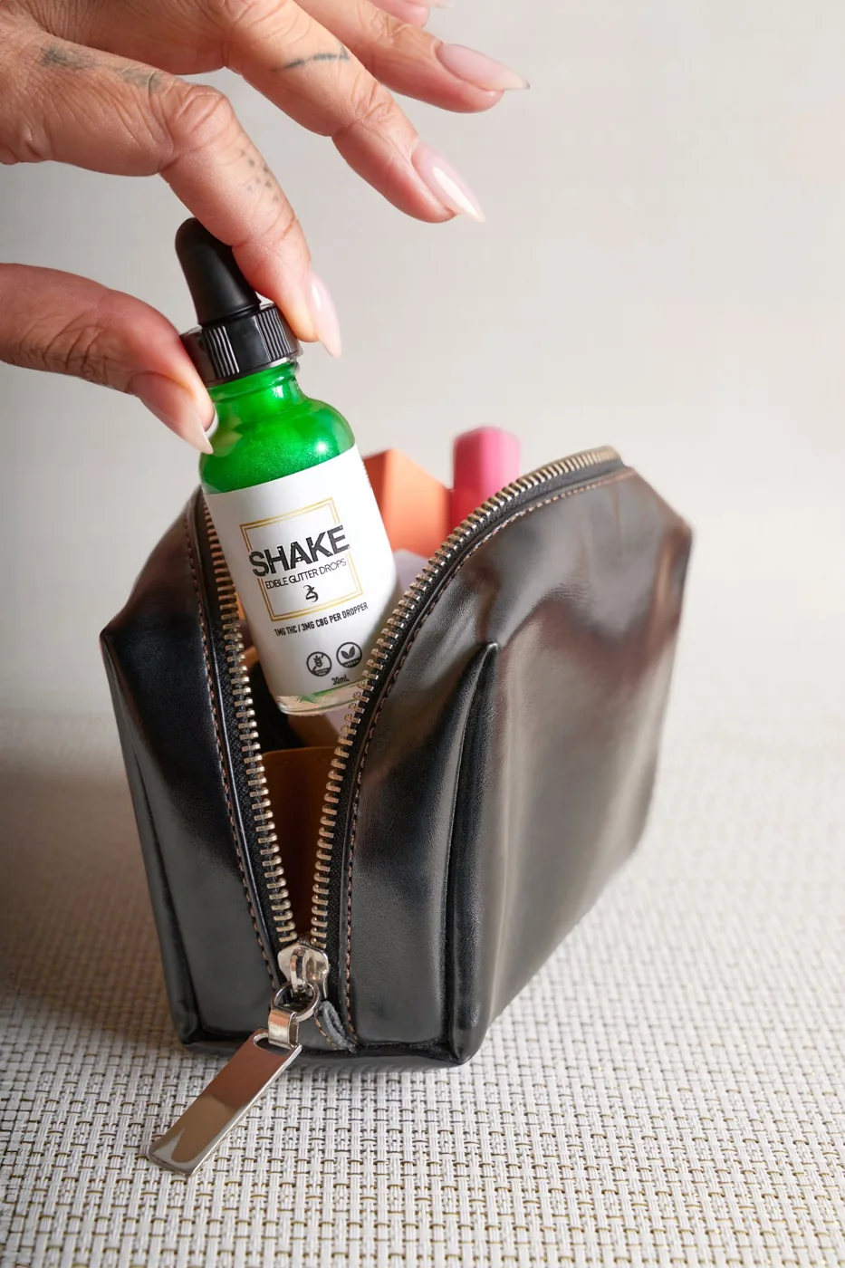 A hand reaching for a dropper bottle in a cosmetic bag