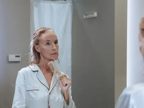 Person combing wet hair while looking into a bathroom mirror
