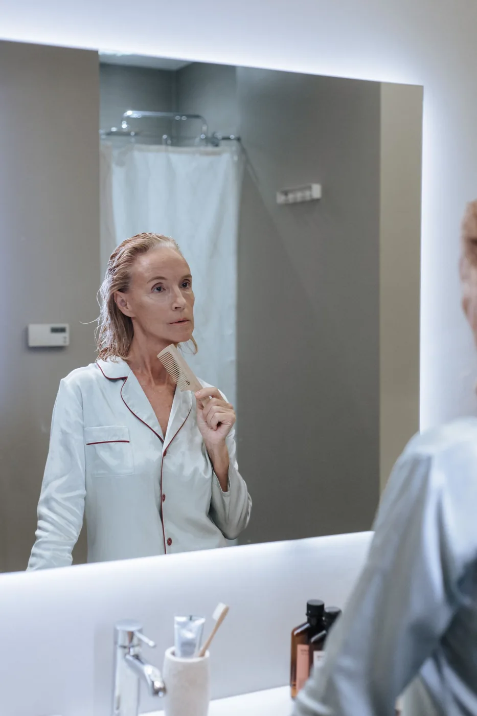Person combing wet hair while looking into a bathroom mirror